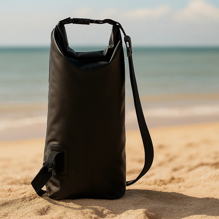 Black dry bag with phone pouch on a sandy beach with ocean in the background