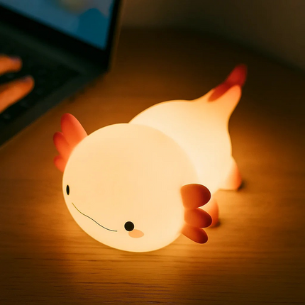 Light-up axolotl toy on a wooden surface with a blurred laptop in the background