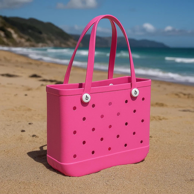 Pink tote bag with perforated design on a sandy beach with ocean and mountains in the background eva